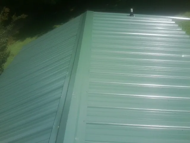 New green metal panels meeting at the ridge of a roof — Flat Roof Repair work by our crew in Akron